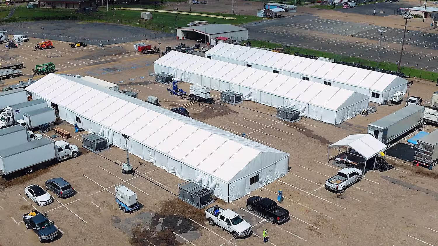 Aerial shot of 3 long tents with trucks backing up to them