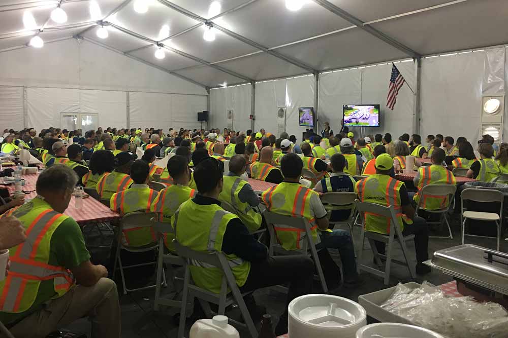 Workers conference with a crowd of people in reflective vests listening to a speaker
