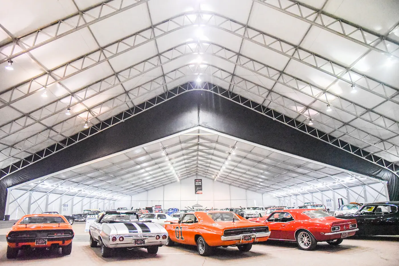 A well lit tent with fancy cars for a car show