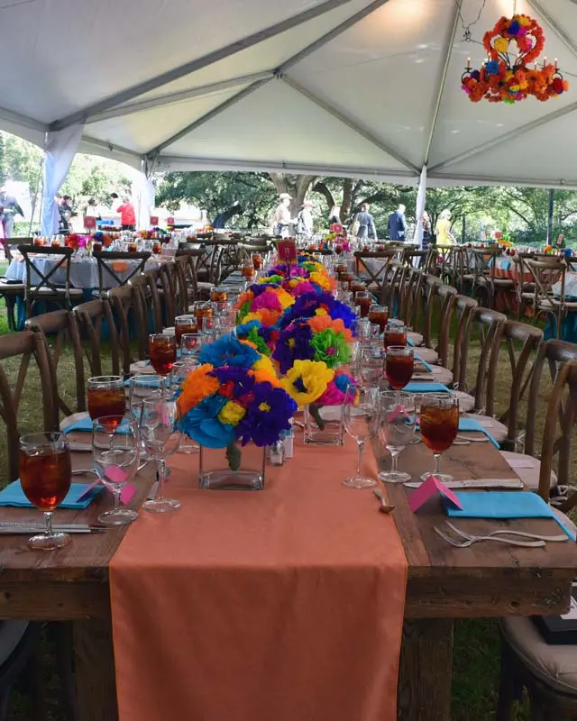 Party table decorated with an orange runner and colorful flowers.