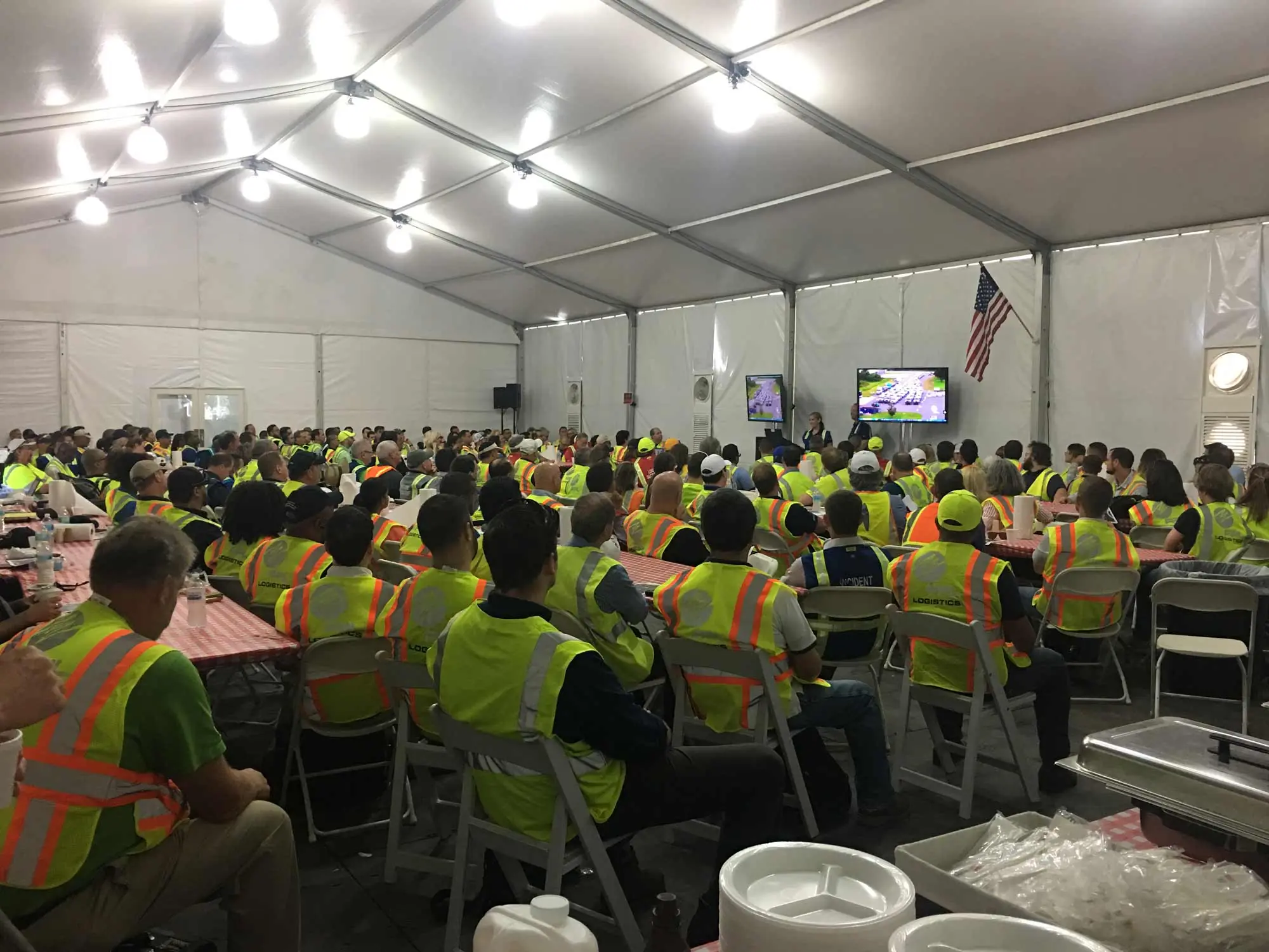 Workers conference with a crowd of people in reflective vests listening to a speaker