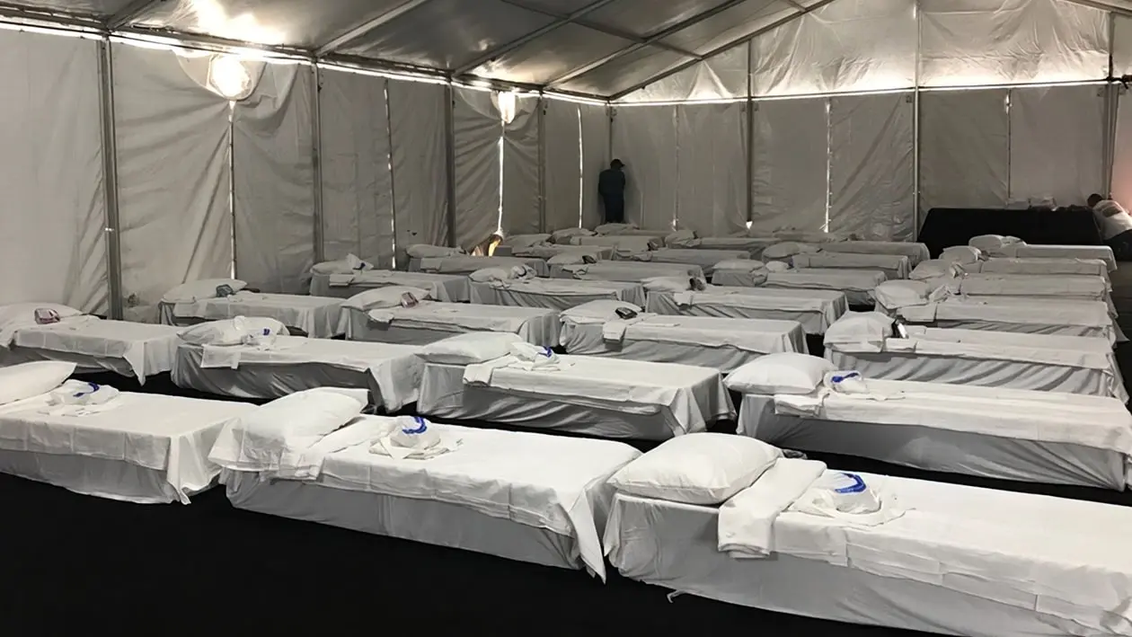 simple beds in rows all with white linens under a big tent
