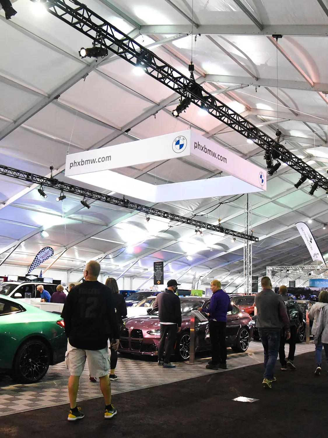 Big open tent with lighting and people looking at cars 