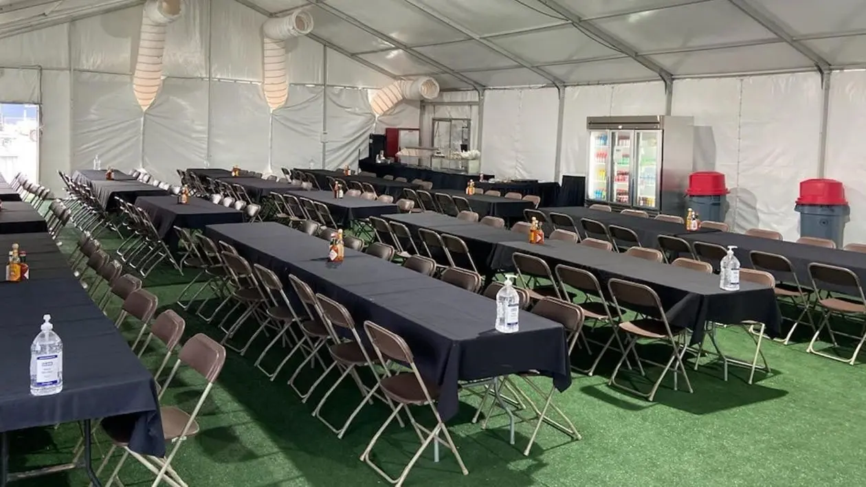Black tables and chairs set up on green floor inside large tent structure