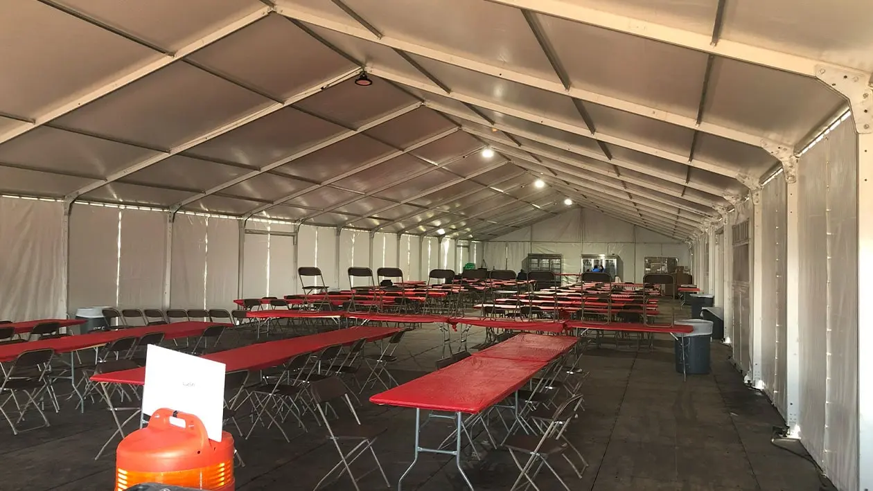 Rows of long red pop up tables with black chairs underneath a large tent structure